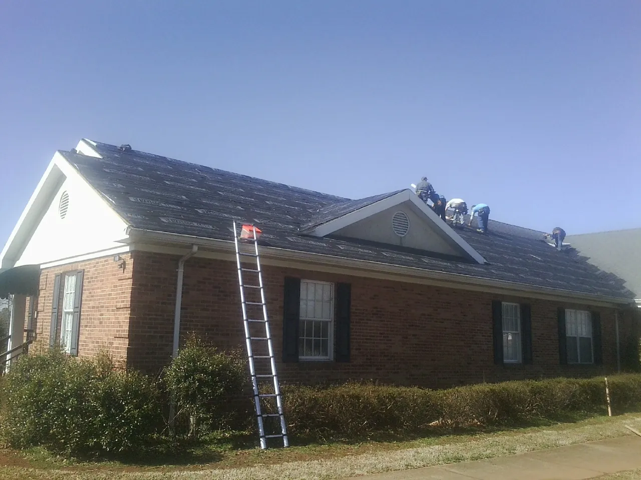 Crew tearing shingles off a brick ranch roof with a ladder set — Metal Roof Repair work by our crew in Randolph